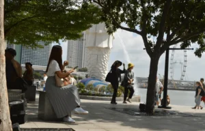 A woman in a wedding dress sits on a bench outdoors, surrounded by trees.